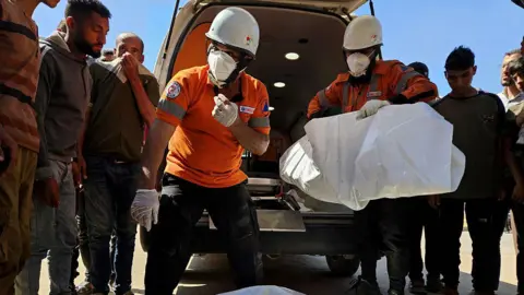 Getty Images Civil defense teams carry the body of a Palestinian following an Israeli airstrike on residential areas in central Khan Yunis, southern Gaza, on May 23, 2025.