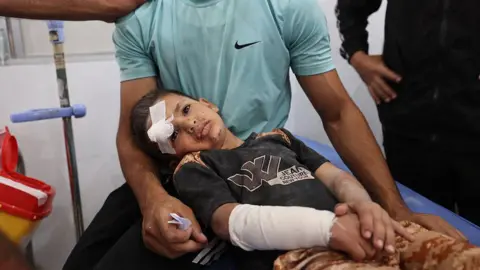 AFP A man comforts a wounded child after receiving treatment at a hospital in Nuseirat refugee camp, central Gaza (19 May 2025)
