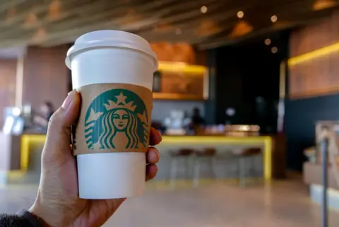 Getty Images Hand holding a coffee cup in a Starbucks coffee shop