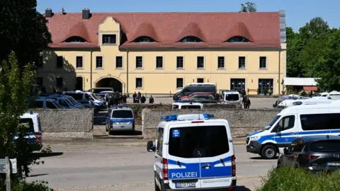 Reuters Blue-and-white police vans are parked outside a large German building with a yellow facade