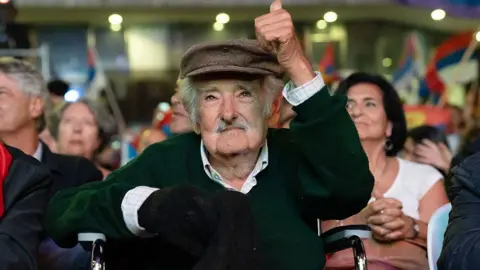 AFP/Getty Images Former Uruguayan President José Mujica gives a thumbs up while sitting among a crowd at an event earlier in 2025