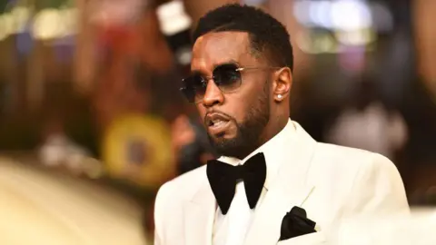 Getty Images Sean "Diddy" Combs photographed in 2021. He wears sunglasses, a white tuxedo with a large black bow tie and matching pocket handkerchief.