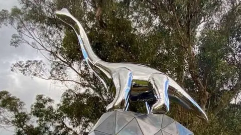 Love Taupō A steel dinosaur sculpture stands on top of a geometric ball in New Zealand.