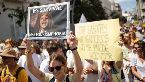 Getty Images A woman wearing sunglasses holds up a sign that reads: It's Survival, Not Tourismphobia