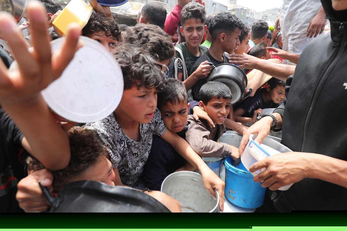 Palestinians queue to receive hot meals distributed by charity organizations amid the ongoing Israeli attacks and blockade, in Nuseirat camp, central Gaza on May 13, 2025. [Moiz Salhi - Anadolu Agency]