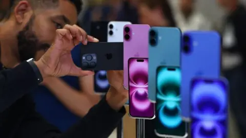 Getty Images Man looking at iphones that are on display in a range of blue green and purple colours