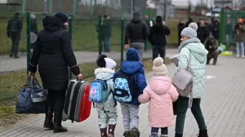 EPA Three young children hold hands with their backs to the camera as a woman looks down at them and a man on the other side carries two bags