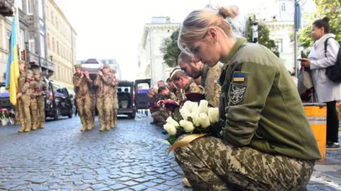 Getty Images Kneeling Ukrainian soldiers mourn a comrade killed in Russia's full-scale invasion