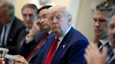 Getty Images Trump is shown in a blue suit and red tie, with a sceptical look on his face, during a cabinet meeting, seated next to Secretary of State Marco Rubio and Secretary of Defence Pete Hegseth 