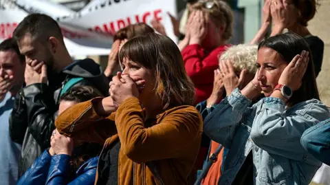 Getty Images Men and women outside a courthouse in France hold their hands over their mouths in protest
