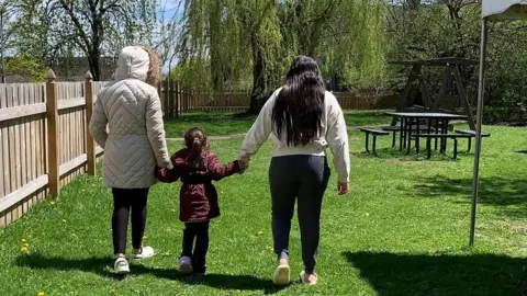 Submitted photo Aracely and her two daughters link hands in a park - we only see them from their back