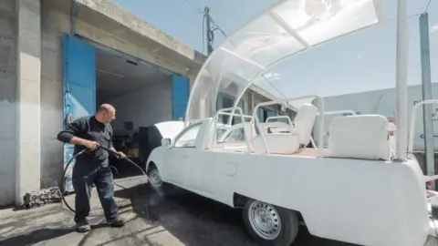 Caritas Jerusalem A man with a power hose works on the popemobile at a garage.