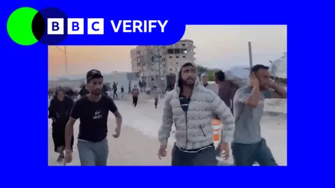 BBC Gazans running after the Israeli strike on Khan Younis. Three men can be seen in the image. One man is wearing a grey jacket, the others are wearing t-shirts. A damaged building can be seen in the image.