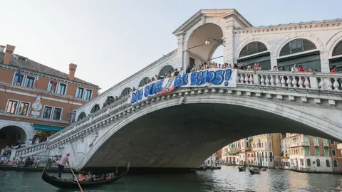 Stefano Mazzola/Getty Images A big sign that says "no space for Bezos" is hung on a bridge in Venice that goes over a canal. There is a gondola sailing through the space under the bridge.