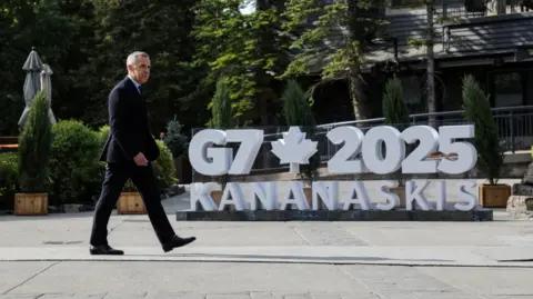 Reuters Canadian Prime Minister Mark Carney walks by a large sign for the G7 summit in Kananaskis during the G7 Leaders' Summit in Alberta, Canada