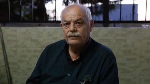 BBC Kasem Abu al-Hija sits in a vigil for his family members. He is a man in his 60s with a grey moustache