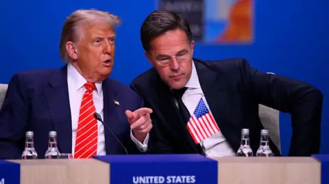 JOHN THYS/AFP US President Donald Trump (L) in a blue suit speaks to NATO Secretary General Mark Rutte in a darker suit and leaning towards him at the start of a NATO leaders summit in The Hague,