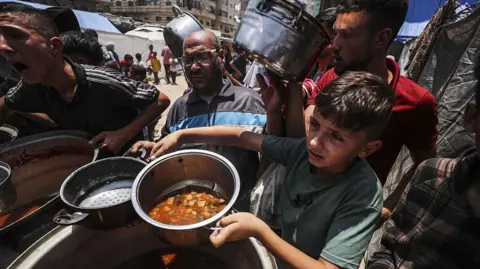 Getty Images Palestinians wait in line to receive hot meals distributed by charity organizations while Israel's destructive attacks continue on 7 June, 2025.
