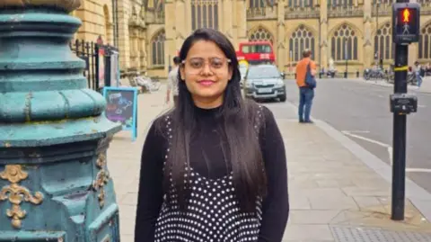 Bhoomi Chauhan Bhoomi Chauhan missed her flight to London due arriving late at Ahmedabad Airport. Bhumi is posing for a photo next to the backdrop of a city centre landmark, next to a navy lamppost and a pelican crossing