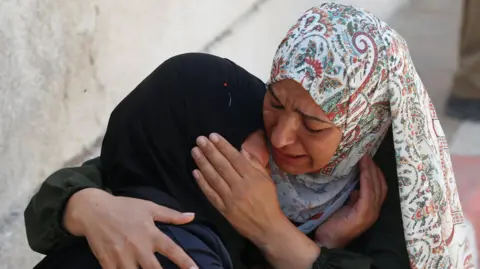 Reuters Two women hold each other as they cry. One woman holds the other woman's head to her shoulder.