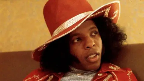 Getty Images Sly Stone wears a red hat and red jacket embelished with rhinestones.