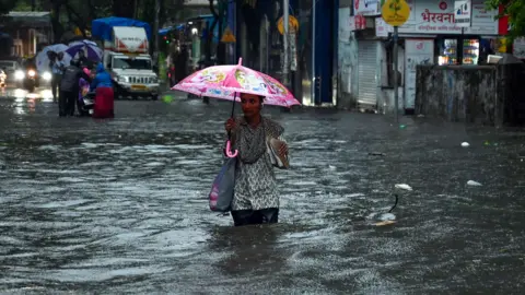 Getty Images People wade through a waterlogged road at Gandhi Market in the Sion area after heavy rain on May 25, 2025 in Mumbai, India.