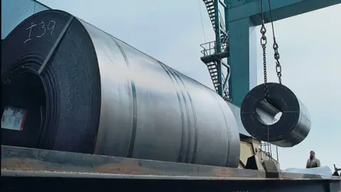 Getty Images Workers use a crane to load a 60,000 pound coil of steel from Holland onto a railroad car for shipment to Ford Motor Company in Ohio from a warehouse at the South Jersey Port Corporation, March 6, 2002 in Camden, NJ along the Delaware River.