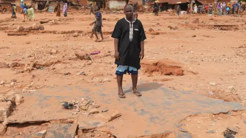 Gift Ufuoma Adamu Yusuf standing on rubble