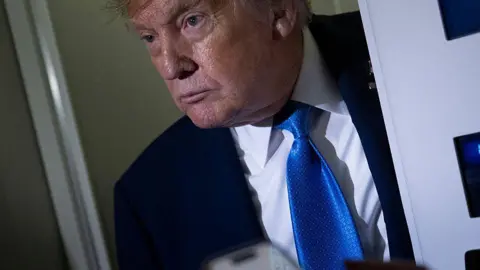 Getty Images Trump wears a blue tie and pokes his head through a door on Air Force One to speak to reporters while returning from G7 meetings in Canada