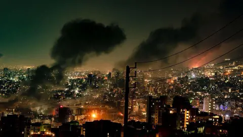Getty Images Tehran's skyline at night on Sunday 15 June, with three large plumes of smoke rising above the city and two large fires blazing below