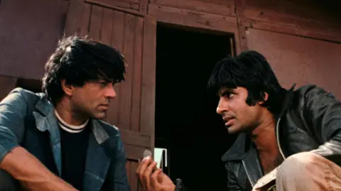 Sippy Films The image shows the two leading men of Sholay Amitabh Bachchan (right) and Dharmendra (left) wearing jackets and engaged in a conversation.