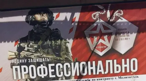BBC A poster in red and white shows a Russian soldier holding a gun and wearing combat gear ready for battle