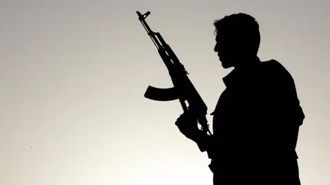 MUSTAFA OZER/AFP via Getty Images) A PKK fighter holding an assault rifle silhouetted against the Sun