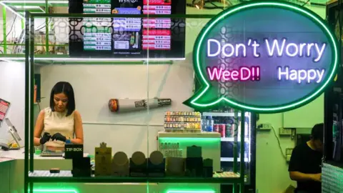 Reuters A brightly-lit neon shop window shows a woman in black gloves working surrounded by cannabis products