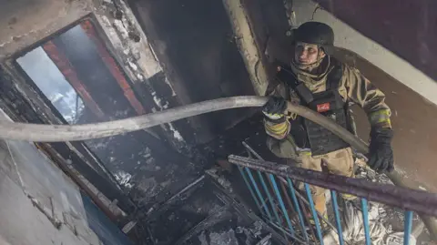 Getty Images Ukrainian emergency service workers extinguish a fire in a residential building, after Russian shelling, in Kostiantynivka