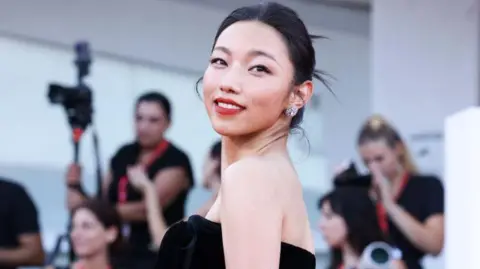 Getty Images Nashi, turning her head, smiling, in a black dress