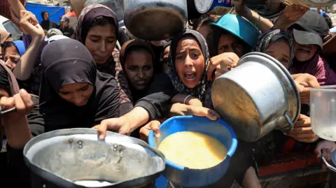 Reuters A crowd of Palestinians push up against each other with their arms outstretched holding pots and buckets, hoping for food