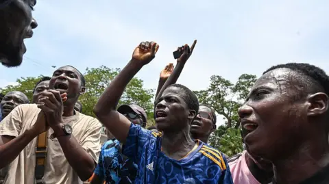 AFP/Getty Images Activists and opposition supporters lift their hands and shout during a protest in front of a courthouse in Abidjan on 2 April 2025 as a hearing was being held regarding the legitimacy of some party leaders, just months before the presidential election. 