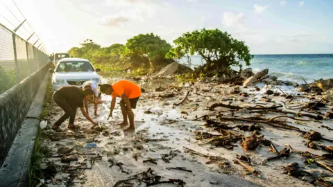 Getty Images A photo taken in 2021 shows high-tide flooding and debris covering the road to the airport in the Marshall Islands capital Majuro. Storms and tidal surges caused widespread flooding, with rising seas blamed for the inundation in the climate-change affected region. 