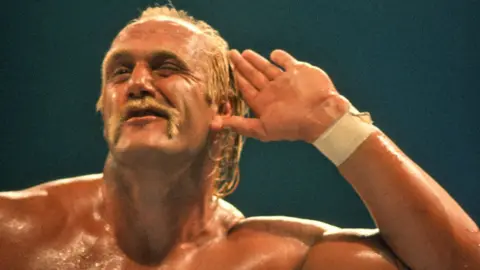 Getty Images A shirtless and sweaty Hulk Hogan after a victory cupping his hand to his ear