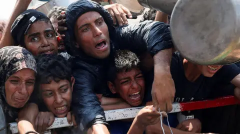 Reuters Palestinians react as they wait to receive food from a charity kitchen