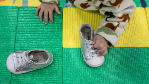 Getty Images Close-up of a baby's hand grabbing a silver baby shoe. The baby is wearing a furry sweater.