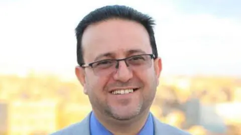 Gaza Ministry of Health A man with short, dark hair and glasses looks into the camera, smiling, in an outdoor photograph
