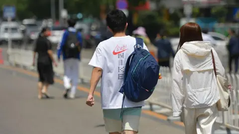 Getty Images Back view of a young man and woman walking side by side on the road on a sunny day.