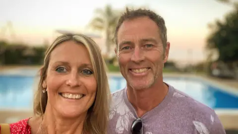Getty Images A man and a woman smile. Behind them is a blurry swimming pool.