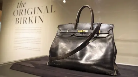 Getty Images A back leather bag in a display case in front of a display manel saying "The original Birkin"