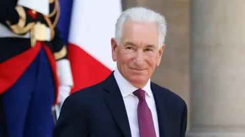 MOHAMMED BADRA/EPA/Shutterstock United States Ambassador to France Charles Kushner is pictured smiling outside the Elysee palace in Paris. He has white hair and is wearing a dark coloured suit, white shirt with a plum coloured tie.