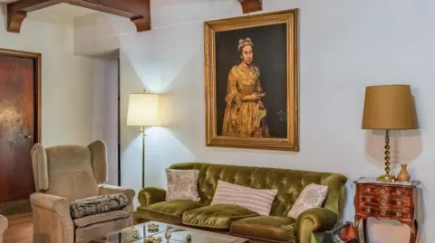 Robles Casas & Campos An interior shot showing a living room with a green sofa against a white wall, flanked by two lamps. A portrait hangs on the wall behind the sofa.