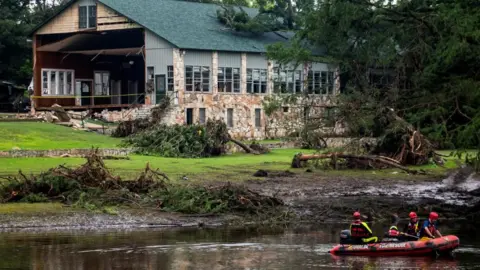 Reuters Search teams in a rubber boat search for flood victims near Camp Mystic, in Texas. A damaged building and blown-over trees are seen behind
