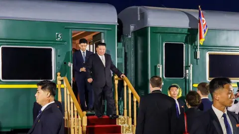 Getty Images Kim Jong Un clutching the railing as he walks down train steps - a green train can be seen in the background.